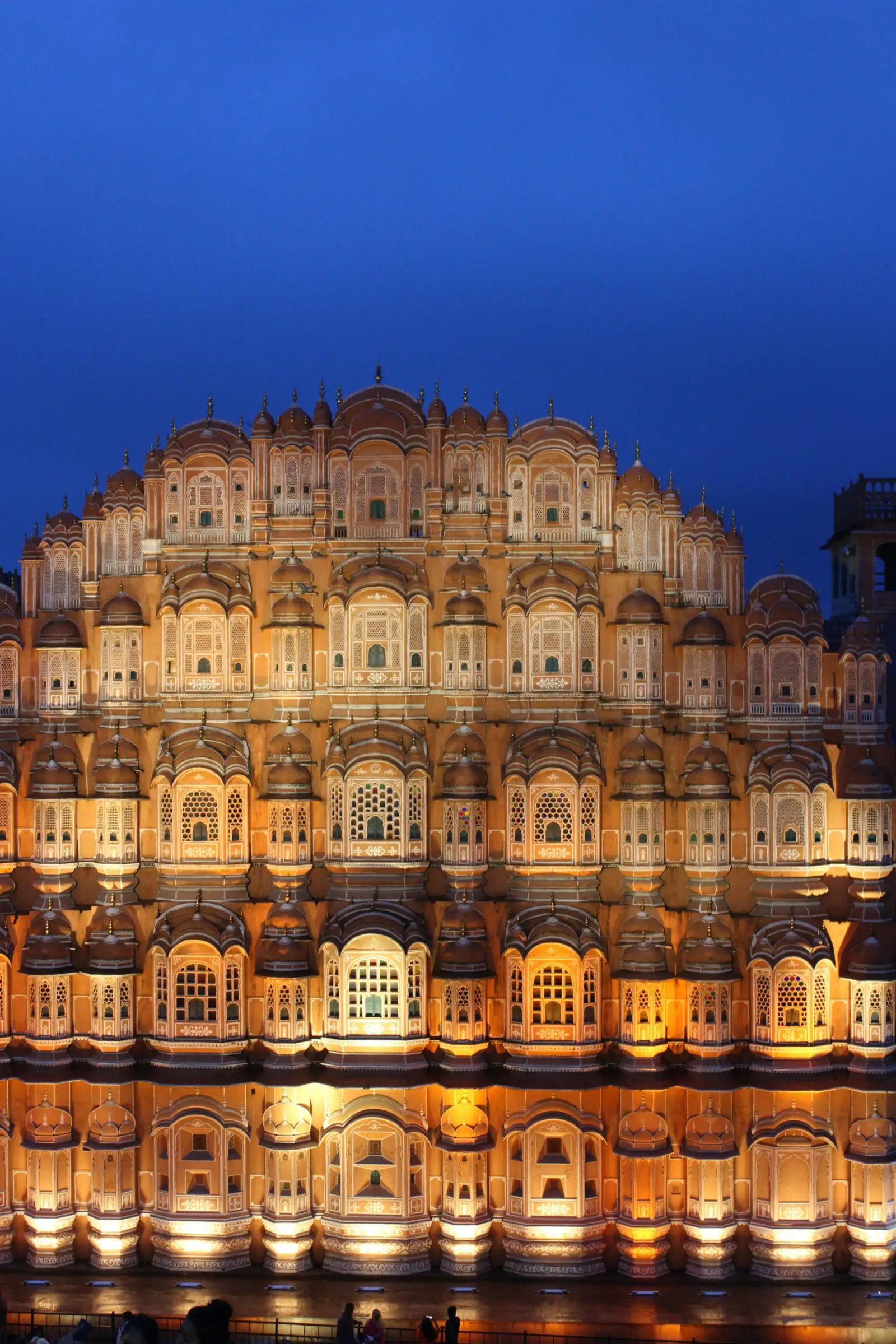 The tiered sandstone façade of Hawa Mahal in Jaipur, lit against a deep blue evening sky.