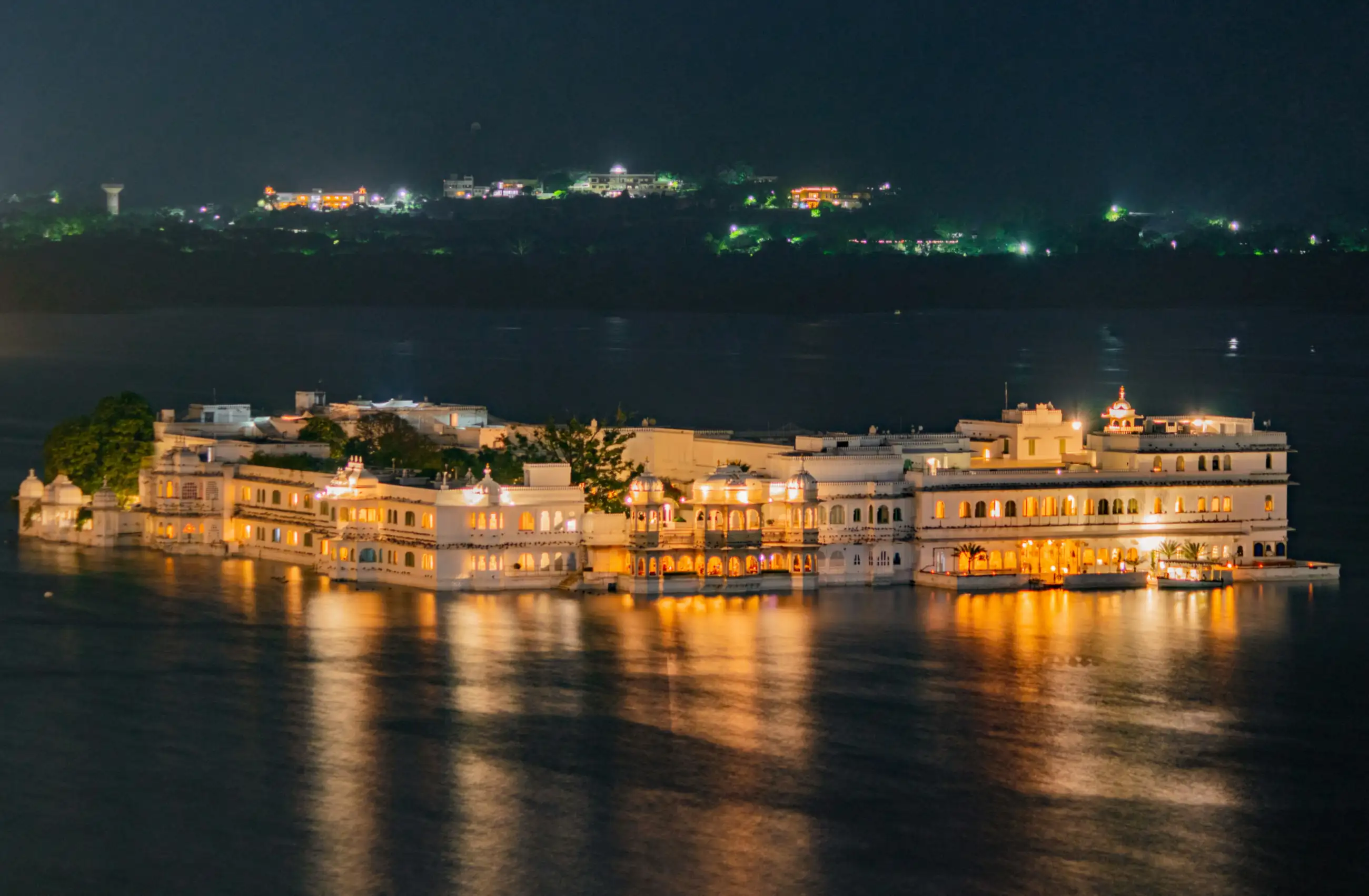 A lit palace on an island in Lake Pichola, Udaipur, reflected in still water at night.