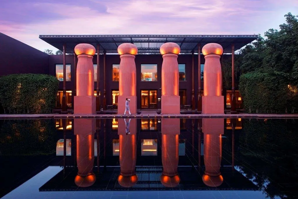 A guest walking between tall red sandstone columns beside a still reflecting pool at dusk.